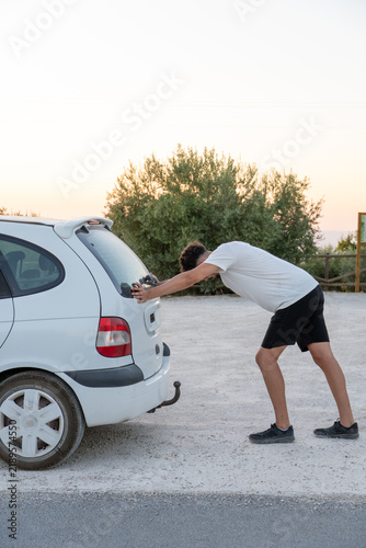 Foto Young man putting effort pushing his broken down car on a dirt road, experiencin