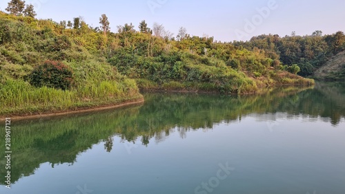Serene lake reflecting lush green hills and forests under a clear sky, capturing the tranquil beauty of nature in a peaceful natural landscape