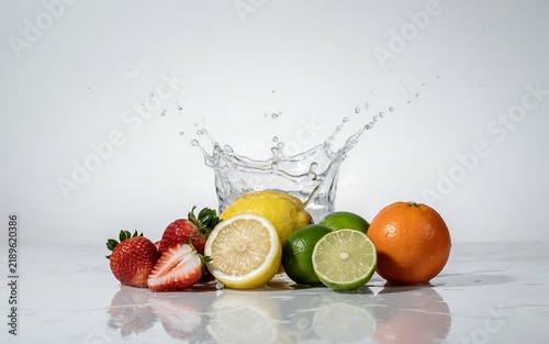 Fresh assorted fruit including strawberries lemon lime and orange with a dramatic water splash on white surface strawberry assorted splashing nutrition refreshing ingredient background