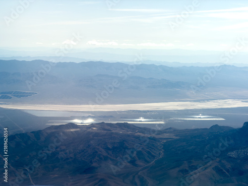 Aerial view of desert mountains overlooking a dry lakebed and glowing solar thermal power plants with mirror fields, Mojave Desert, California