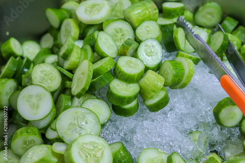 Foto Close up of sliced fresh green cucumbers chilled on crushed ice with stainless metal tongs