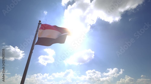 Yemen Flag waving on a Flagpole from a Moving Angle in front of a blue sky with clouds	