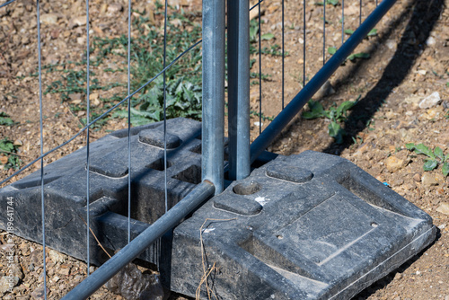 Fotografía A heavy-duty black rubber base block secures portable wire mesh fencing panels upright on dry dirt ground