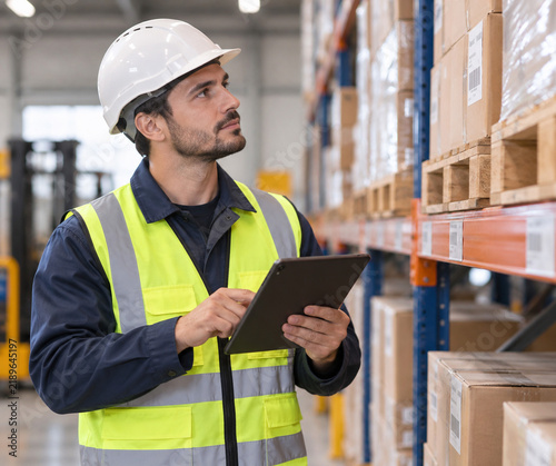 Male Warehouse Worker in Hardhat and Safety Vest Using Tablet PC