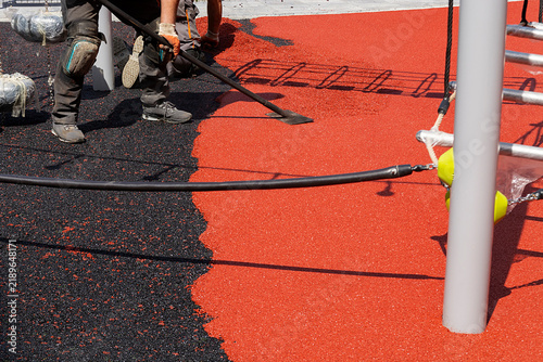 workers spreading material and smoothing surface of future playground for children