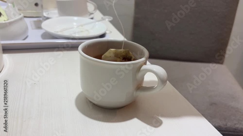 male hand dipping tea bag in hot water at table in hotel