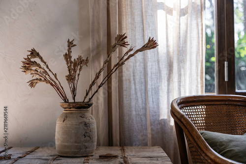Warm tones interior vignette of vase, rattan chair and linen curtain
