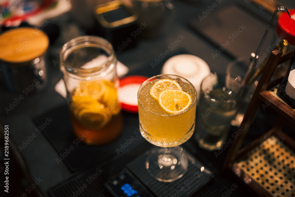 Obraz premium Orange cocktail in stemmed glass on bar counter with citrus garnish, mason jar, and cocktail tools creating warm atmosphere for beverage service and hospitality