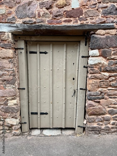 A rustic green wooden door in an ancient stone wall with an aged wooden lintel above. England, UK