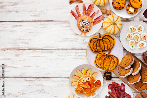 Fun Thanksgiving or fall breakfast or brunch foods. Top down view side border on a white wood background. Pumpkin spice pancakes, loaf, muffins, turkey shaped pancakes and pastry. Copy space.