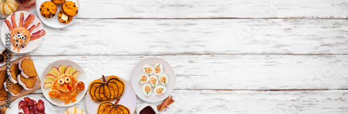 Fun Thanksgiving or fall breakfast or brunch foods. Above view corner border on a white wood banner background. Pumpkin spice pancakes, loaf, muffins, turkey shaped pancakes and pastry. Copy space.