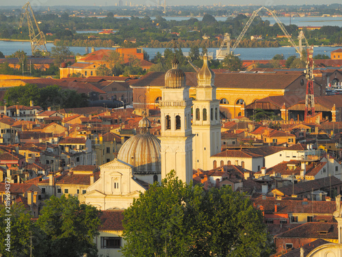 Aerial view of Venice rooftops with white Chiesa di San Giorgio dei Greci church dome and bell tower, industrial cranes in background