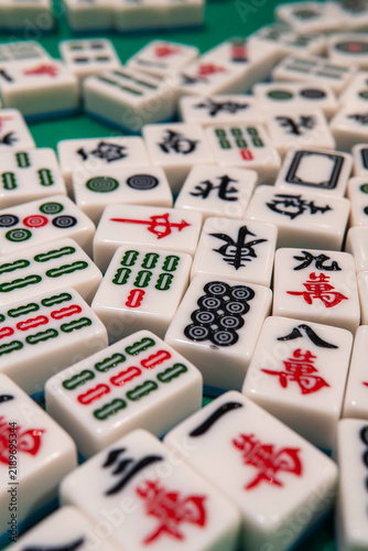 Mahjong Tiles Laid Out: A close-up view of numerous Mahjong tiles, revealing their intricate designs and traditional Chinese characters, arranged on a green surface, ready for a game.