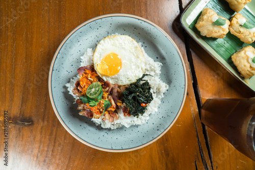 Nasi Campur Delight: A visually appealing plate of Nasi Campur, featuring fluffy white rice topped with a sunny-side-up egg, savory meat, fresh greens, and a hint of chili.