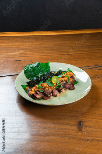 Exotic Culinary Delight: A beautifully presented dish featuring thinly sliced meat with vibrant toppings and a lime wedge, served on a banana leaf, offers a tantalizing glimpse into gourmet cuisine.