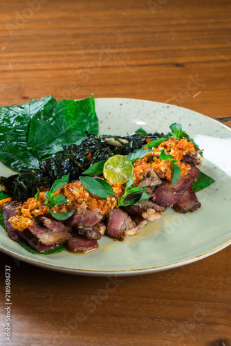 Gourmet Steak Platter: Sliced steak, seasoned and topped with a vibrant chili paste, is presented on a plate with fresh greens and a lime wedge, inviting a culinary delight.