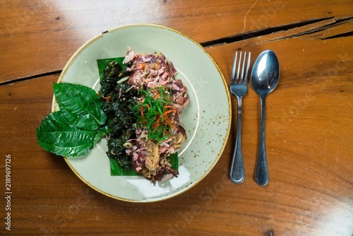 A Culinary Delight: An artfully presented dish featuring vibrant green leaves, tender meat, and savory toppings rests on a textured ceramic plate, accompanied by a fork and spoon.