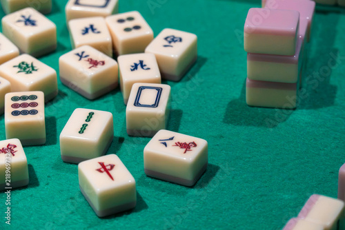 Mahjong Tiles on Felt Table: A close-up view of ivory mahjong tiles with intricate symbols scattered across a green felt table, hinting at a game in progress.