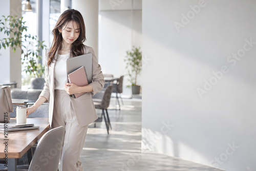 明るいコワーキングラウンジでノートとパソコンを整理する働く女性 自然光と余白を生かしたビジネス向けコピースペース