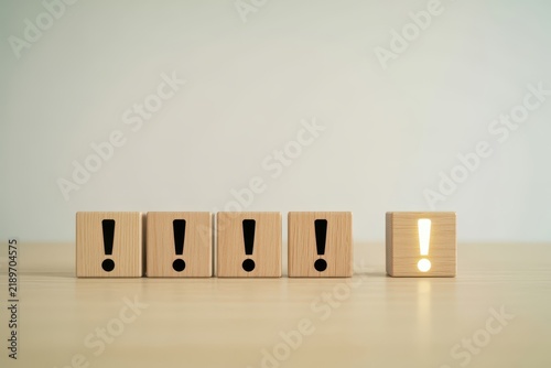 A glowing exclamation mark on wooden blocks among standard ones on a table. Great for problem solving and unique business ideas.