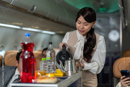 Canvastavla Asian female flight attendant prepares beverage at service cart inside commercial aircraft cabin, supporting inflight drink service, onboard hospitality and professional passenger care experience