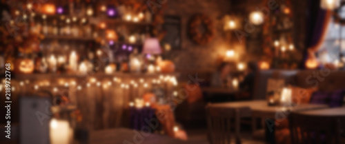 Cozy Halloween café background featuring fully blurred pumpkins, warm lamps, autumn decorations, and soft orange purple bokeh for elegant seasonal designs.