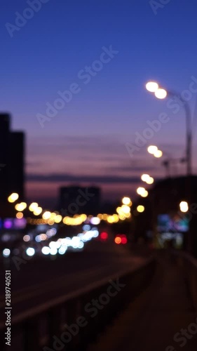 Defocused evening traffic with glowing street lights, blurred vehicle headlights and twilight sky, creating an atmospheric urban background for transportation, commuting, mobility and modern city conc