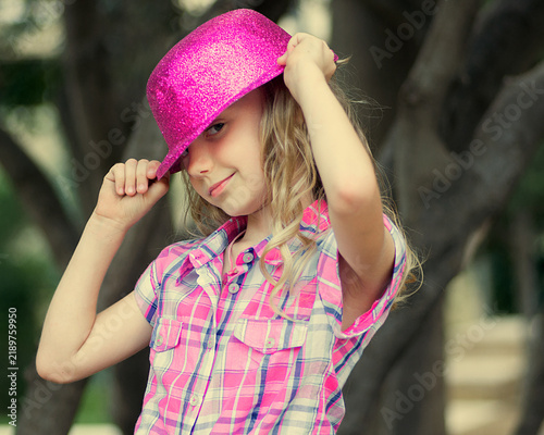 Fotografie Stylish young blonde girl holding a bright pink glitter bowler hat while posing outdoors
