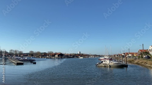 View of Arcachon, France, with small boats along the waterfront and the town's buildings in the background. The coastal scene reflects the maritime character and relaxed atmosphere. 