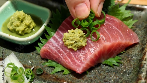 Premium 4K culinary cinematography showcasing perfectly sliced raw tuna sashimi displaying exquisite fatty marbling and rich texture arranged beautifully alongside traditional green wasabi
