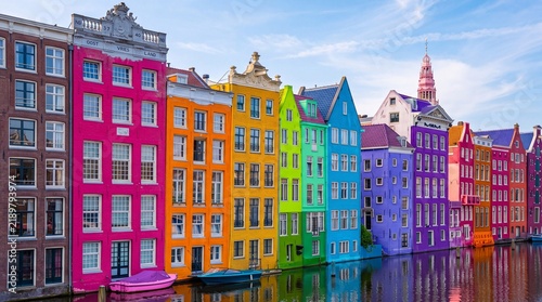 Vibrant colorful historical houses reflecting in a calm canal water surface under a clear blue sky with reflection