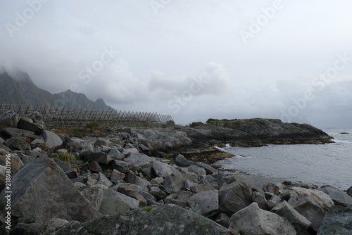 Rocky coastline with waves crashing against stones, distant islands visible under a cloudy sky in Lofoten Islands, Norway during the month of September