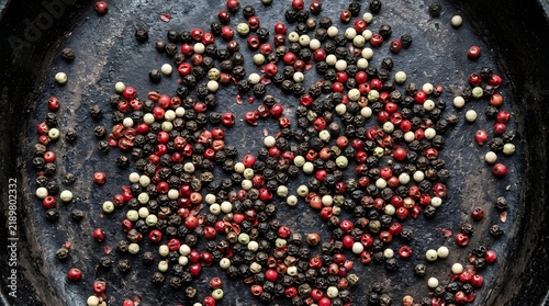 Colorful peppercorns scattered on a dark cast iron skillet overhead view