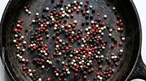 Mixed black white and red peppercorns on a textured dark cast iron skillet