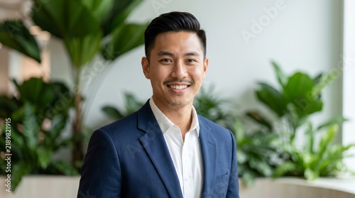 Confident Asian man in a suit smiling in a corporate office setting.