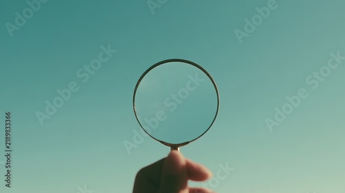 Close-up of a mannequin hand holding a magnifying glass, with copy space on a bright, clean background.