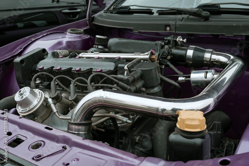 Close-up of a modified car engine bay with chrome piping, valve cover, and purple bodywork