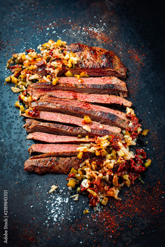 Barbecue roasted dry aged flank steak sliced with relish made of gherkin, onions and sun dried tomatos served as top view on a rustic plate