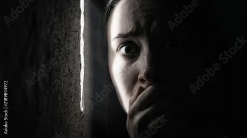 Terrified Woman Peeking Through Crack in Dark Room