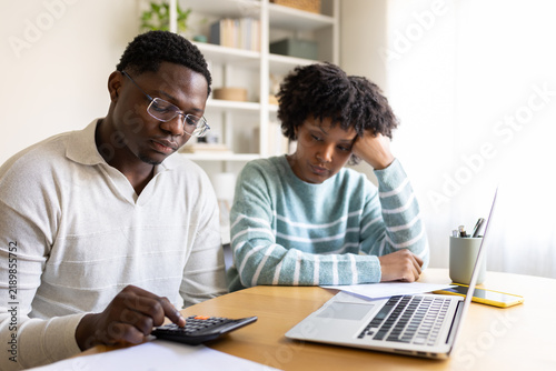 Stressed couple calculating domestic bills at home using calculator and laptop