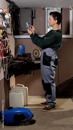 Obraz na płótnie Male mechanic in overalls inspects a small engine carburetor at a cluttered home