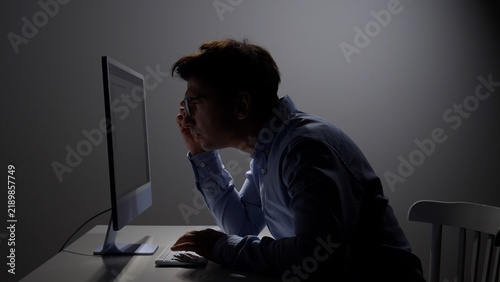 фотографія Man wearing glasses intently focusing on a computer screen in a dark room, worki