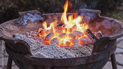 Hot glowing charcoal briquettes burning brightly inside a metal fire pit container during an outdoor gathering