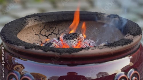 Traditional clay brazier burning hot charcoal with bright flames inside a ceramic vessel outdoors on ground