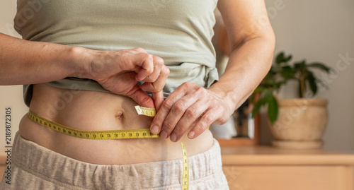 Bild auf Leinwand Close-up, woman measuring her waist with yellow tape measure at home