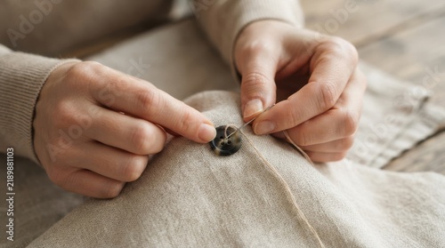 Close-up of caucasian woman hands sewing a button on linen fabric, handmade clothing repair concept