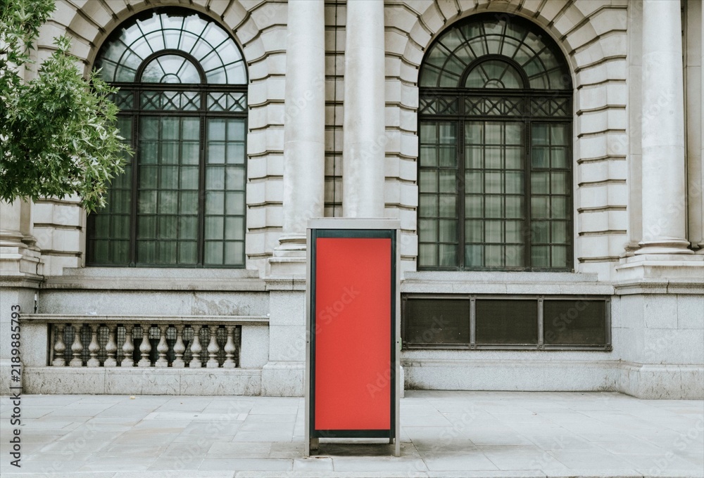 Obraz premium Red advertising kiosk in front of historic stone building