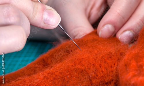 Close up of hands using a felting needle to shape bright orange wool into a soft handmade craft project
