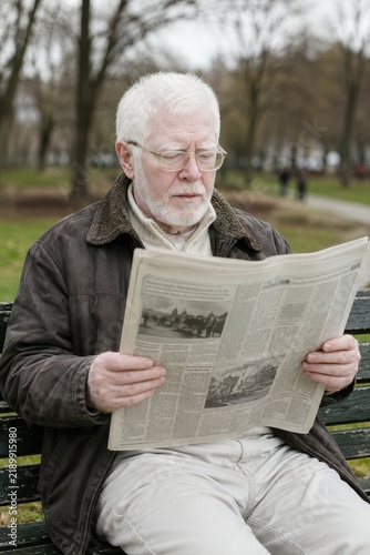 Elderly man with albinism reading newspaper on park bench