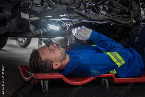 Принти на полотні Man in blue coverall repairing vehicle underside in garage with EV underbody ins